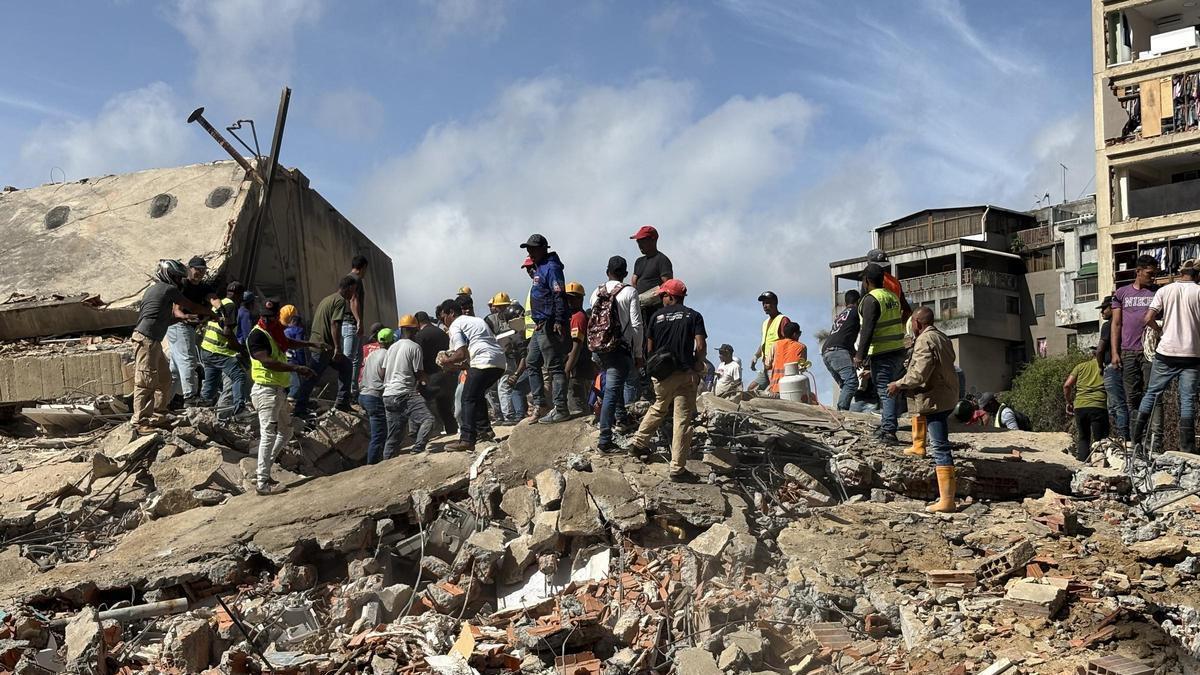 Personas caminan sobre escombros de edificios derrumbados por los terremotos este jueves, en el sector San Bernardino, en Caracas (Venezuela).
