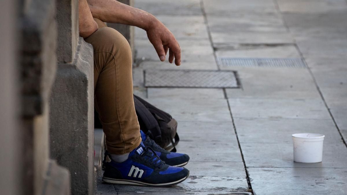 Un hombre pide limosna en la calle sentado en un portal.