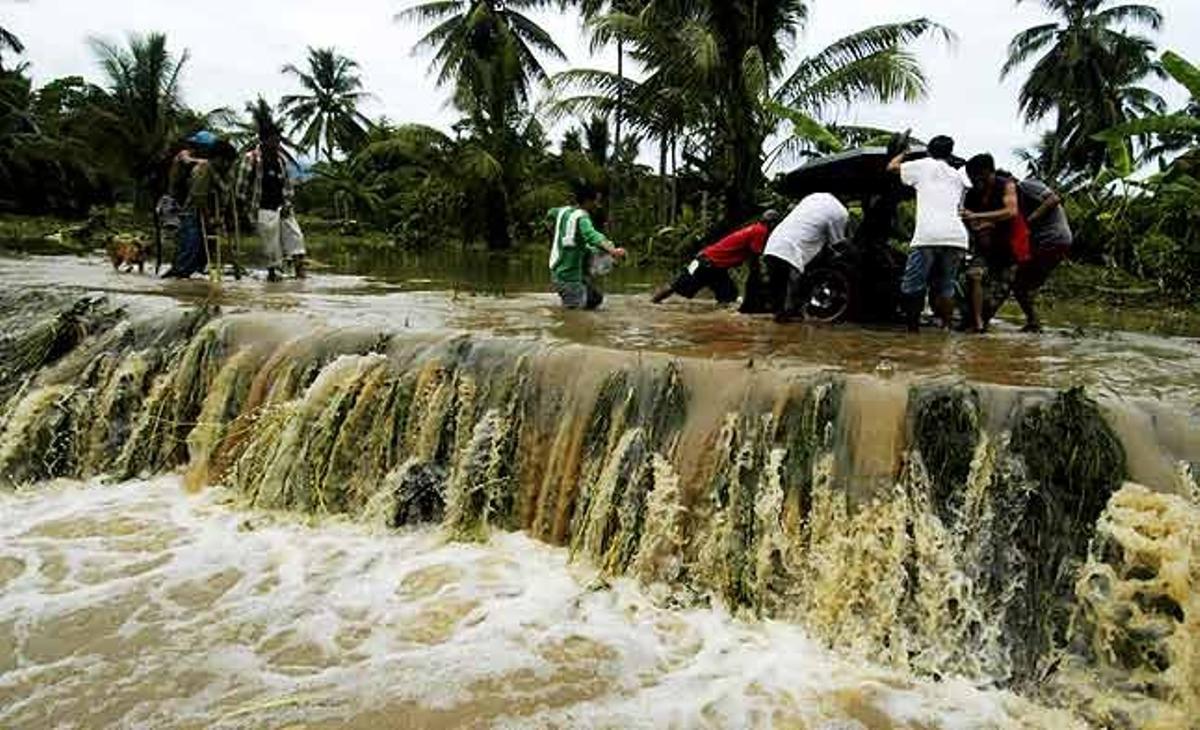 Equips de rescat empenyen un tricicle motoritzat estancat en un camí inundat per les pluges al sud de Filipines.