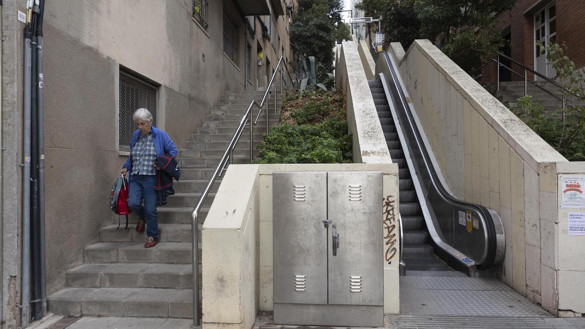 Una mujer baja los escalones junto a un tramo de escalera mecánica estropeado en la Baixada de la Glòria, en el distrito de Gràcia de Barcelona.