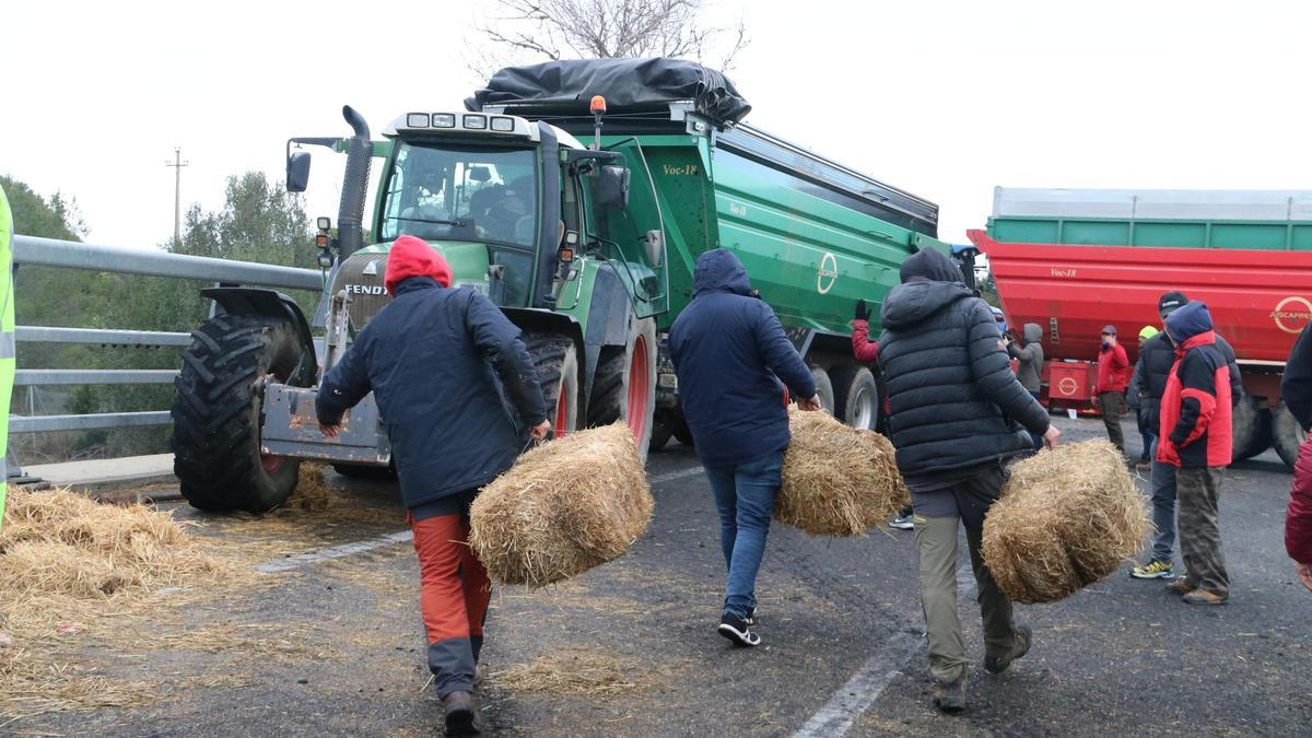 Un grup de pagesos portant bales de palla per obstaculitzar la via.