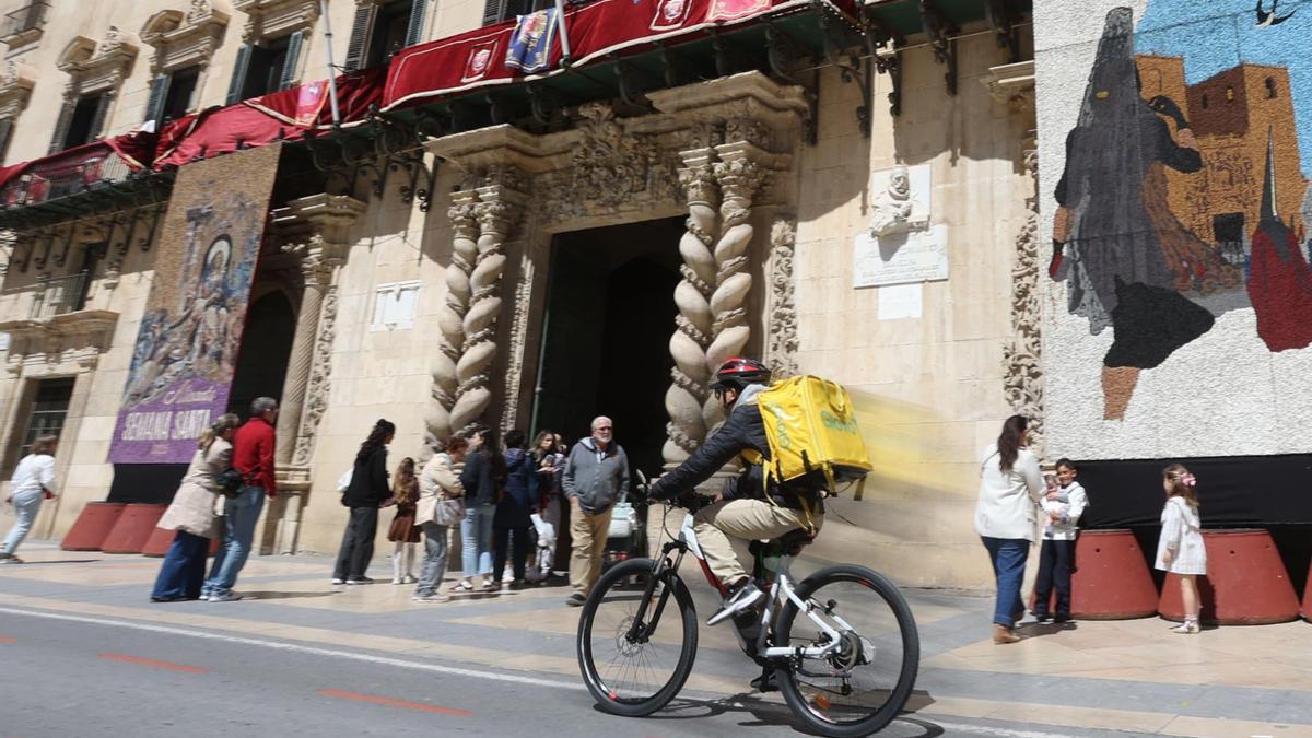 Un «rider», ayer, durante su jornada de trabajo, pasa por la puerta del Ayuntamiento de Alicante.