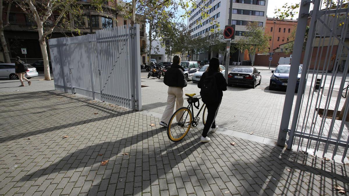 Dos jóvenes atraviesan la valla que rodea la plaza Mercè Sala, en Barcelona.