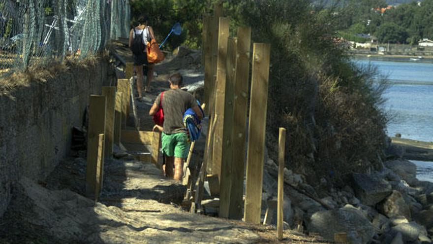 Bañistas de A Ladeira pasan entre los maderos al no existir señalización de obras.