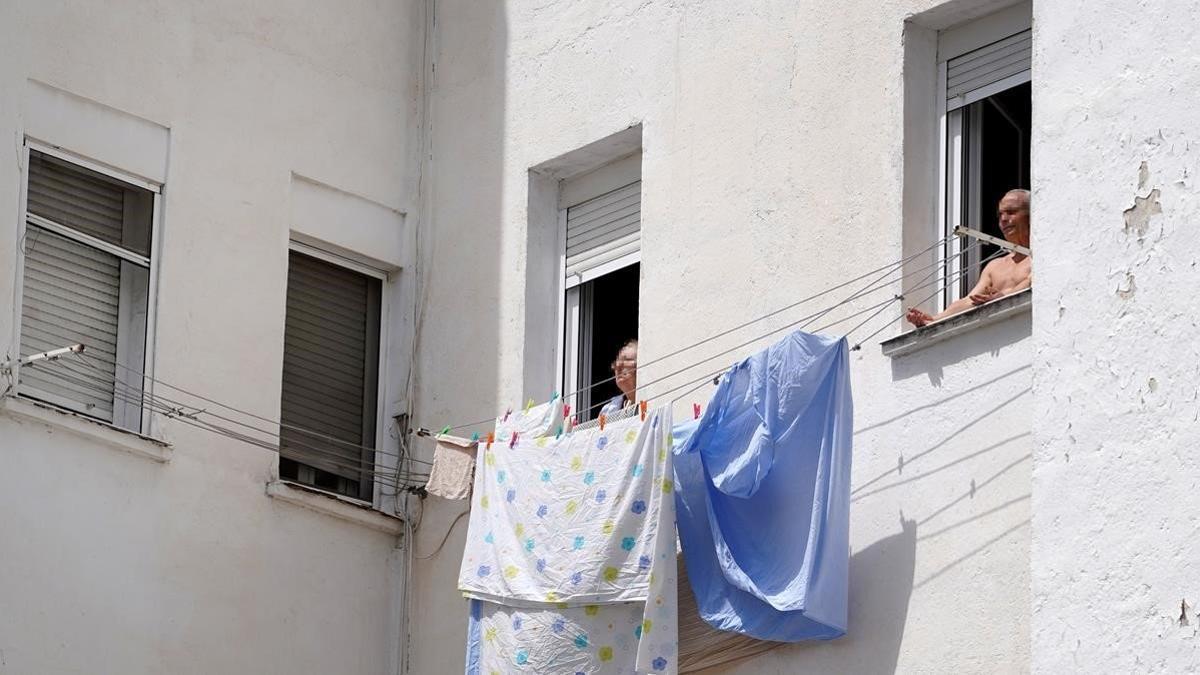 Dos personas mayores toman el sol en la ventana vivienda en Madrid.