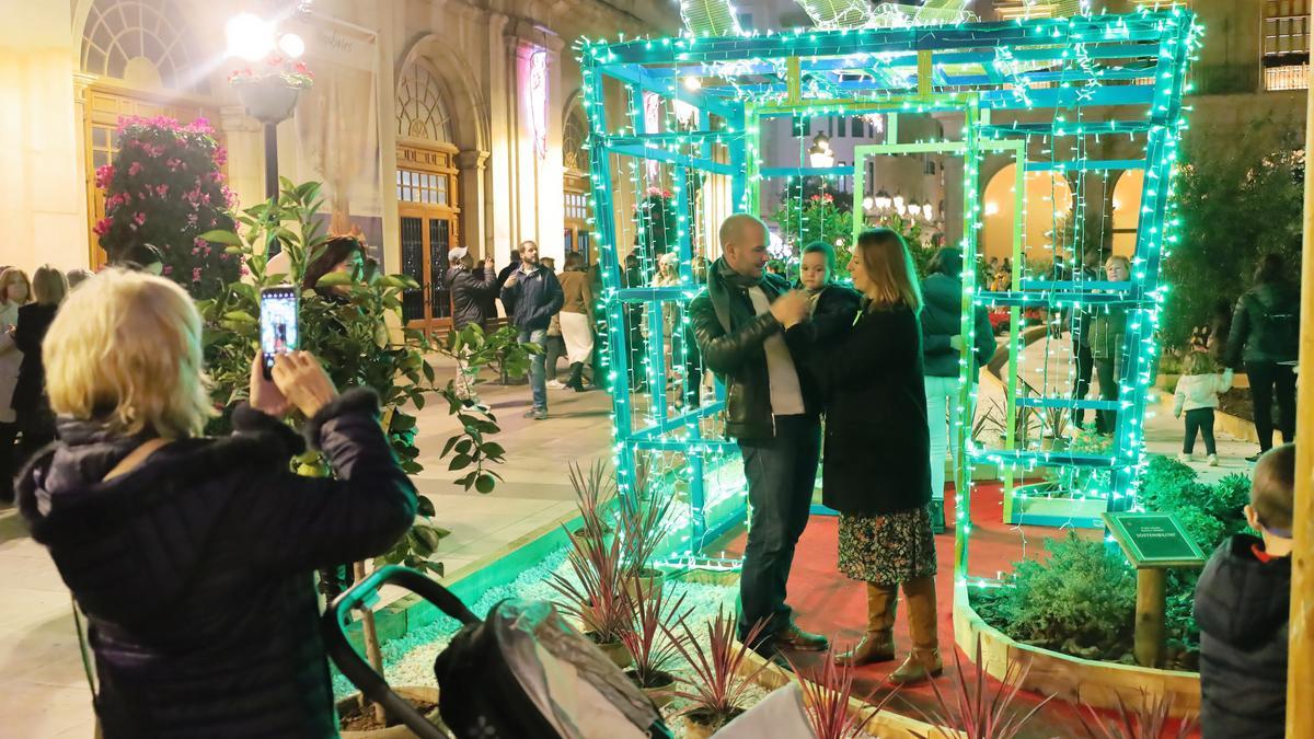 Una pareja posa con su bebé junto al regalo iluminado.