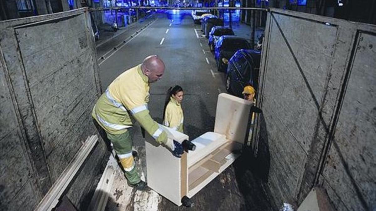 El equipo de recogida municipal de trastos formado por David, Melanie y Sergio sube al camión un mueble.