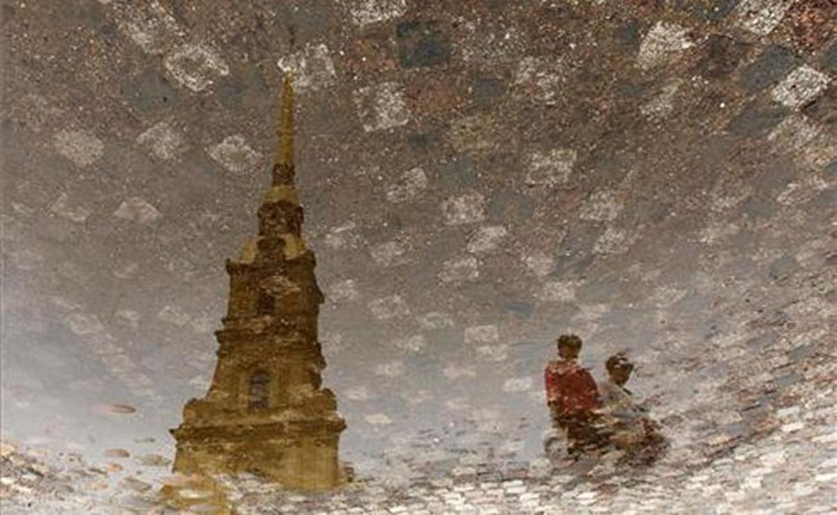 Les siluetes de dos turistes es reflecteixen en un bassal davant de la fortalesa de Sant Pere i Sant Pau, a prop de Sant Petersburg (Rússia).
