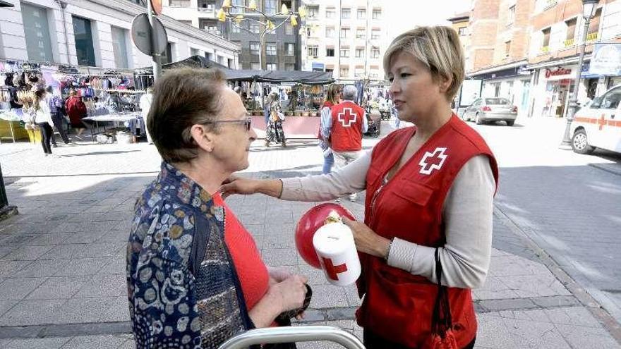 Sobre estas líneas, Soledad González entrega un donativo a Elia Arciniegas en La Felguera. Arriba, voluntarios de Cruz Roja, en una mesa.