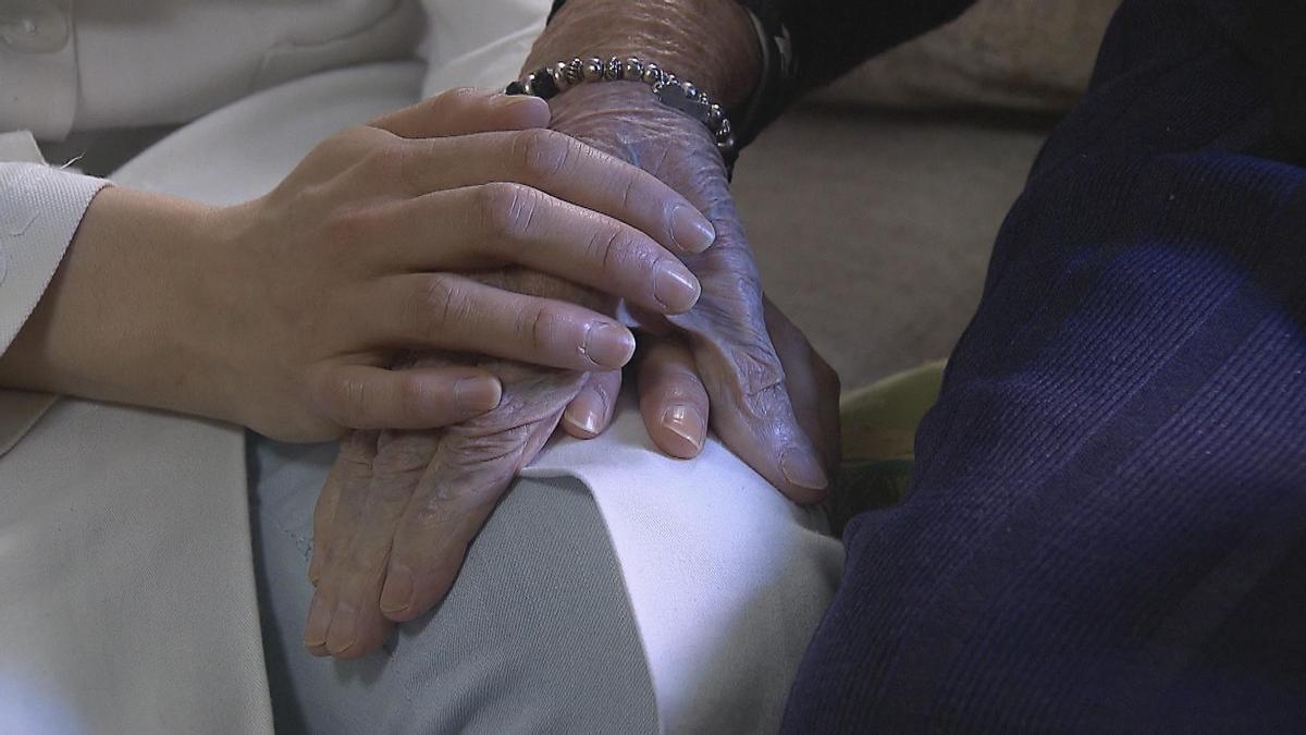 Una sanitaria coge la mano de una abuela en un centro sanitario.
