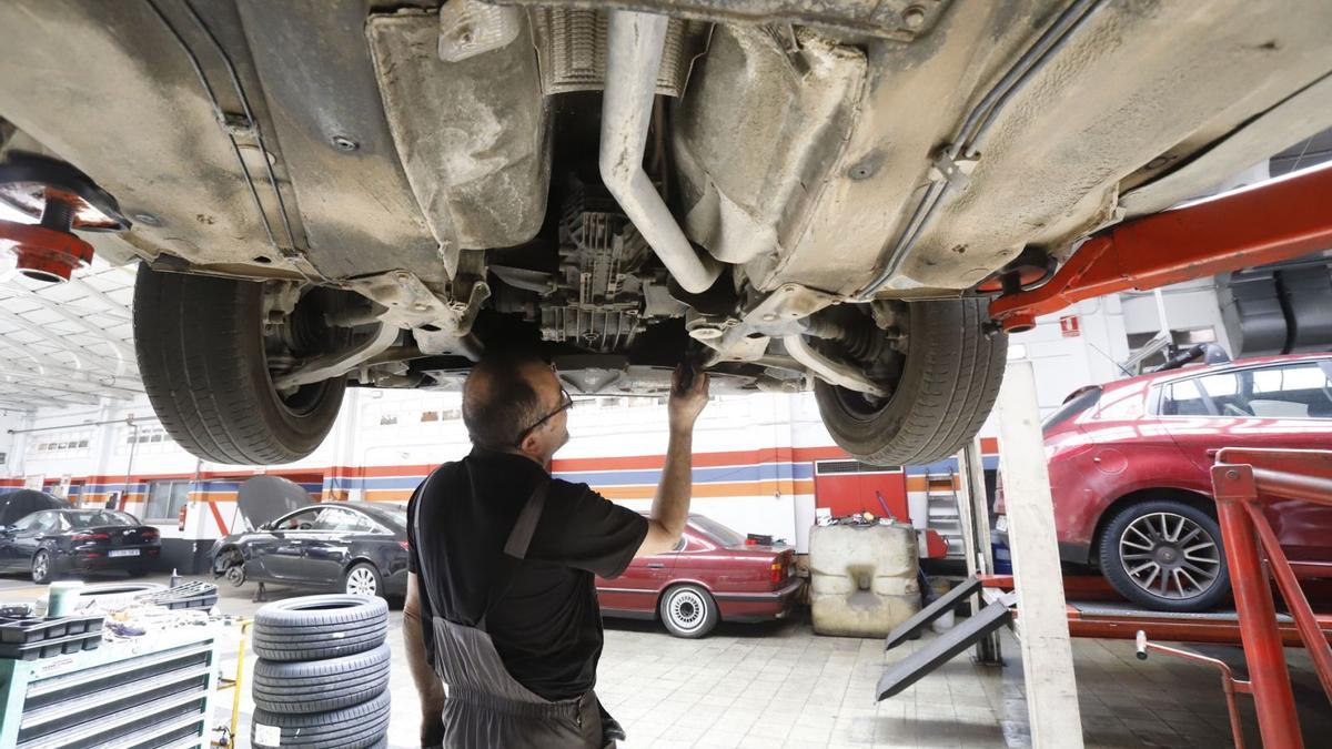 Ariza, mecánico en un taller de Zaragoza, revisa el catalizador de un automóvil situado en la parte frontal del mismo.  | ANDREEA  VORNICU