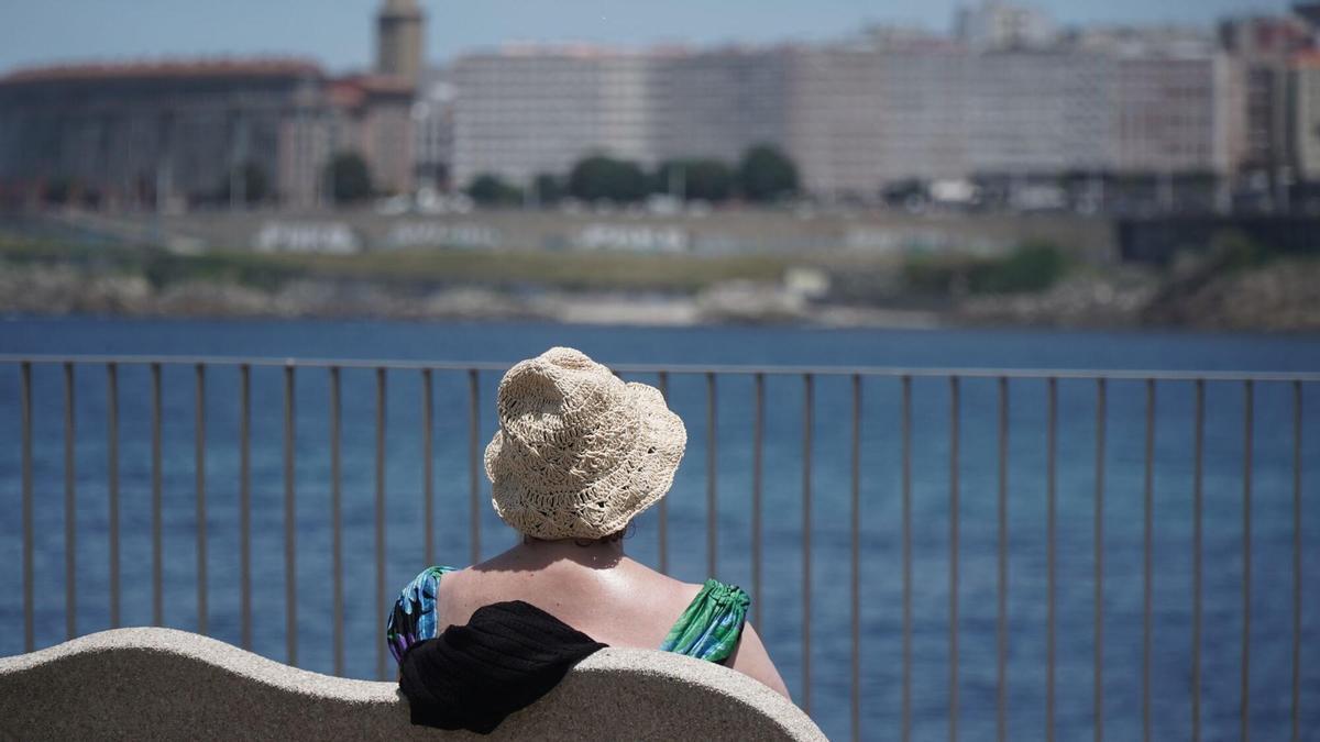 Una mujer se sienta en un banco al sol frente a la playa de Riazor