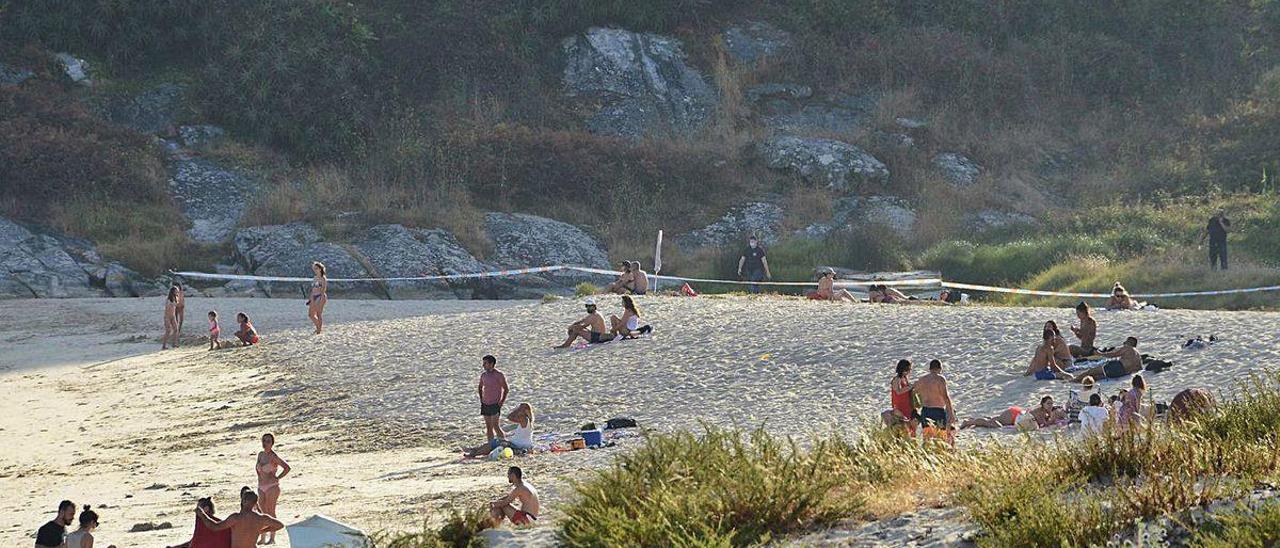 Usuarios de la playa fuera del agua y recogiendo sus cosas. Al fondo, la zona del vertido balizada.