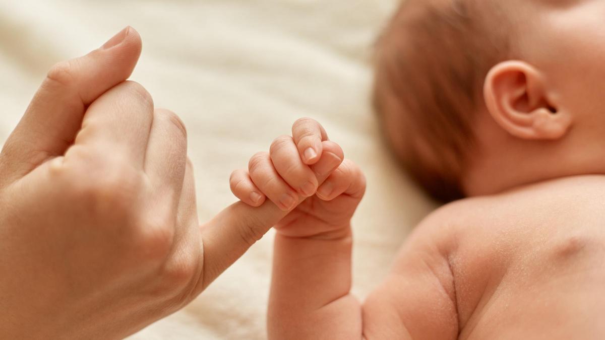 Un recién nacido agarrando el dedo de su madre.