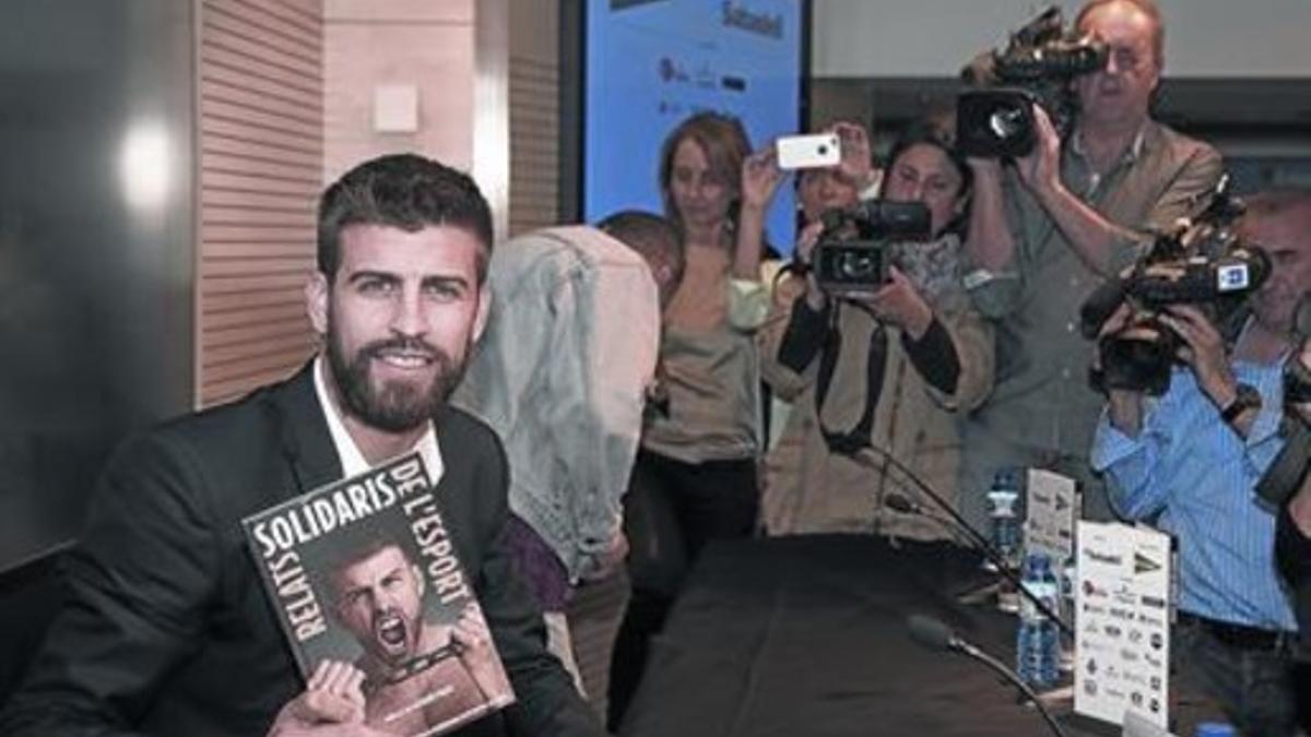 Piqué enseña el libro que él apadrina en esta décima edición, ayer en la sede de Banc Sabadell.