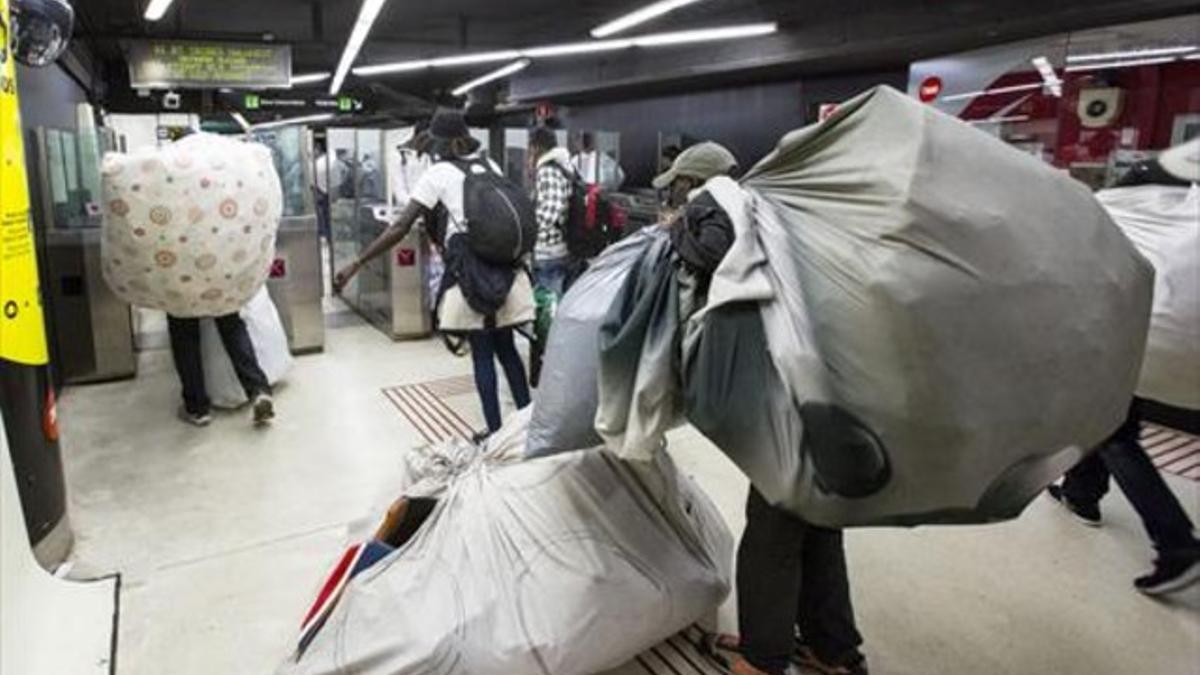 Vendedores ambulantes ilegales cargan sus pesados fardos esquivando la presencia policial, ayer en Drassanes.