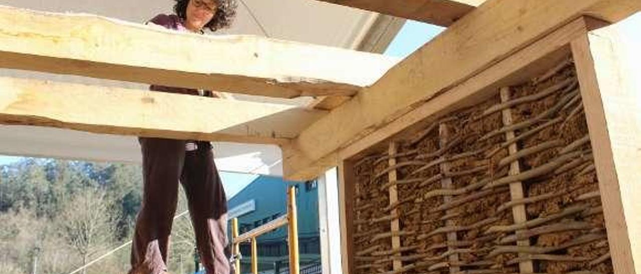 Karina Pérez trabaja en la cubierta. A la derecha puede verse la estructura de una de las paredes, con un trenzado de madera y barro.