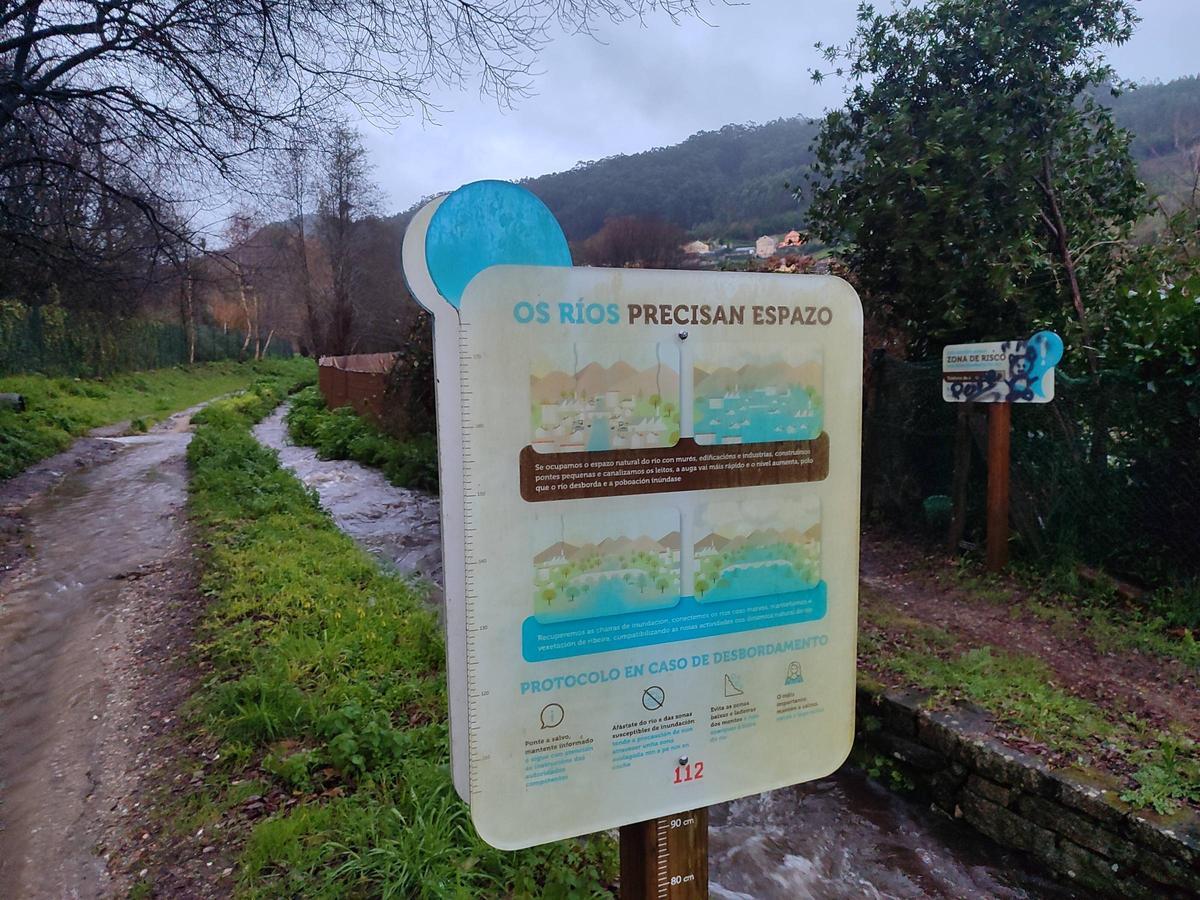 Un cartel de Augas de Galicia, sobre la crecida de los ríos, al lado del cauce del Bispo, que ayer bajaba con mucho caudal.