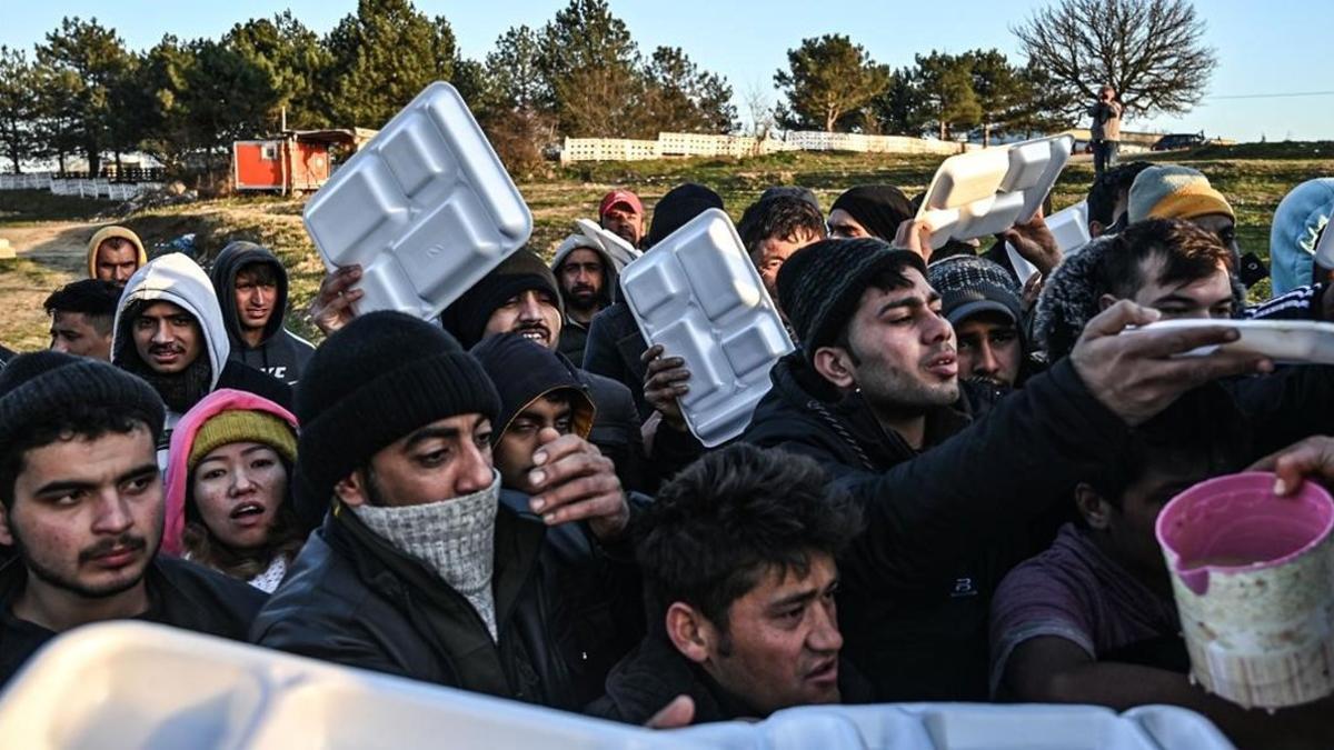 Un grupo de migrantes esperan que les sirvan comida en teritorio turco mientras esperan cruzar el río Meritsa para entrar en Grecia.