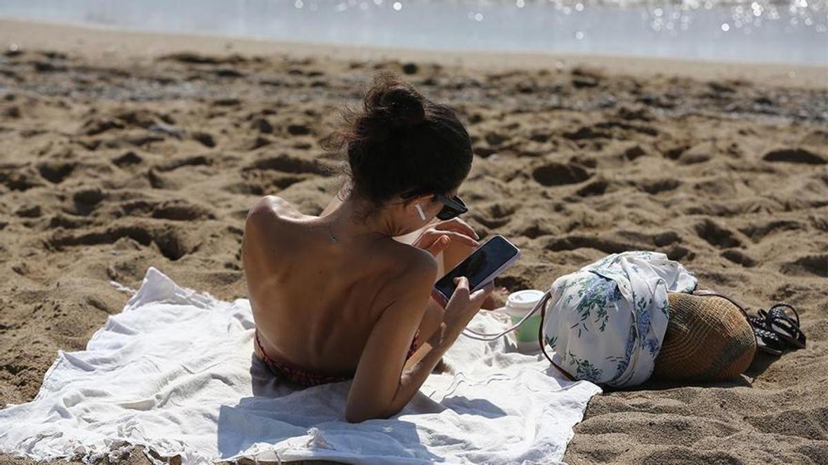 Una chica mira el móvil en la playa.