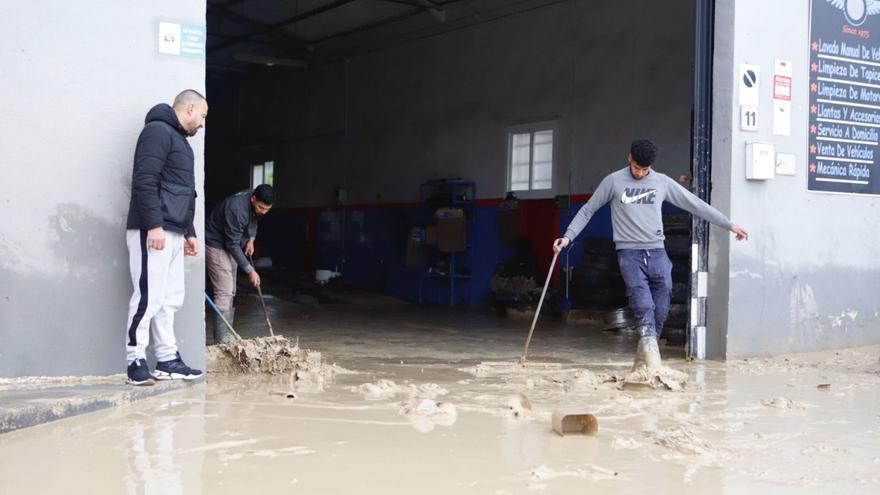 Los trabajadores de un taller mecánico de Lorca se afanan en retirar los lodos generados por las lluvias.