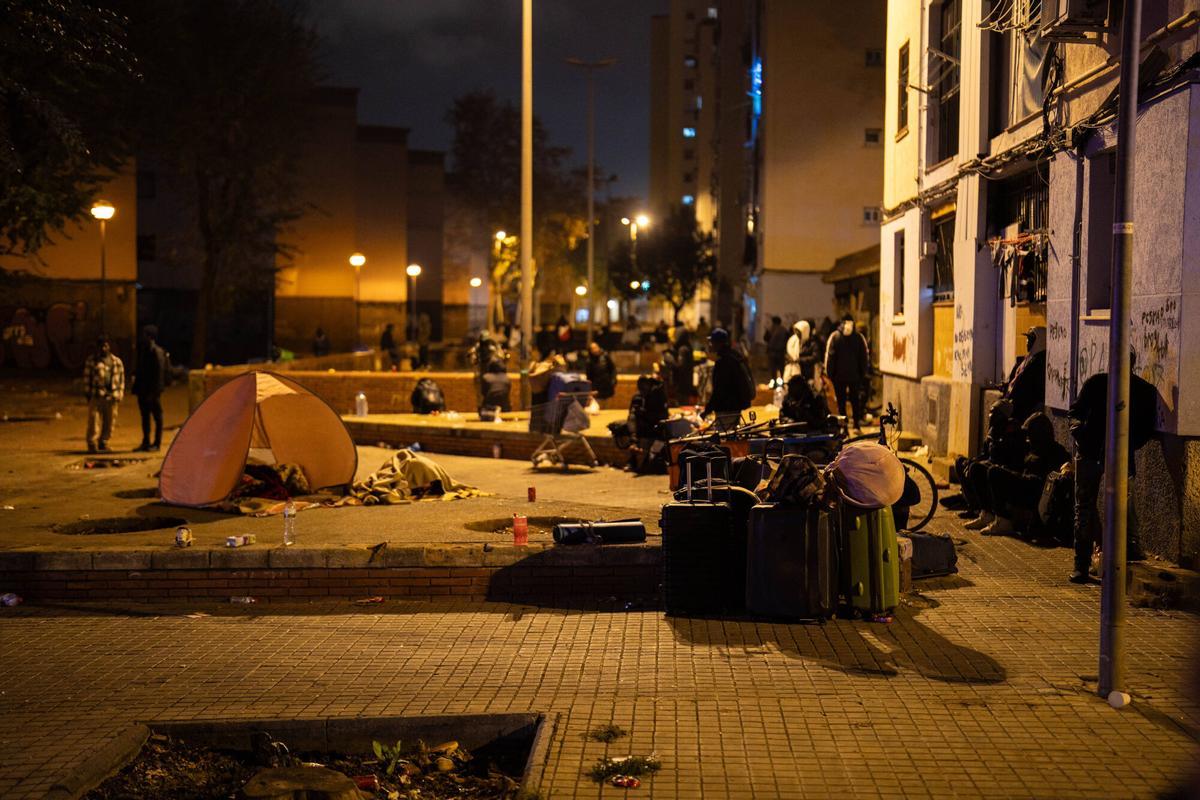 Badalona, 17/12/2025. Sociedad. Personas desalojadas del antiguo instituto B9 se concentran en la plaza frente al edificio, preparando enseres y refugios improvisados para pasar su primera noche durmiendo en la calle tras el desalojo. Foto: Zowy Voeten / El Periódico