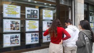 Tres jóvenes miran anuncios inmobiliarios en un escaparate de Madrid.