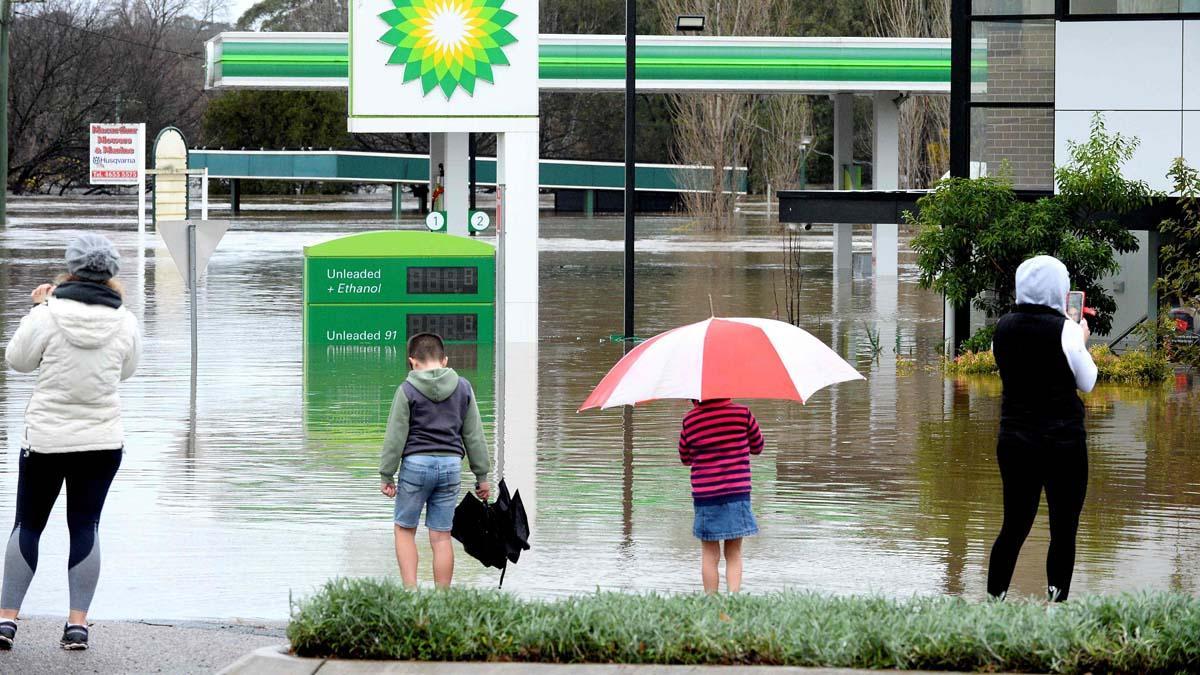 La gente se para junto a una gasolinera inundada debido a la lluvia torrencial en el suburbio de Camden en Sydney .