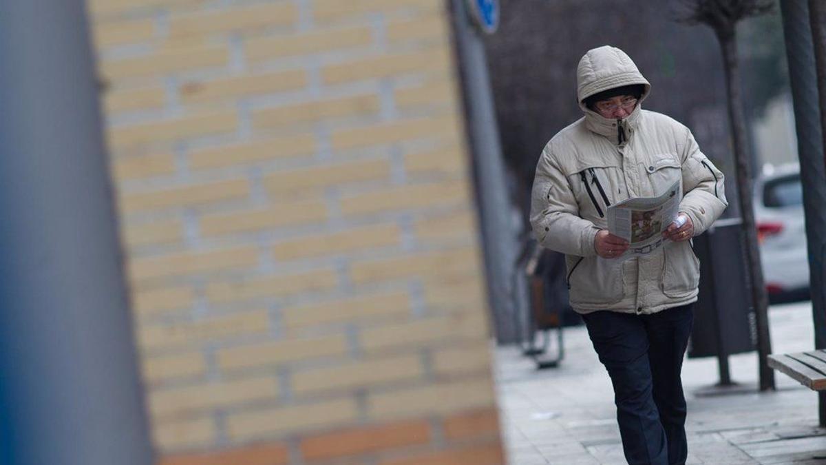 El frío es Una persona camina abrigado contra el frío.