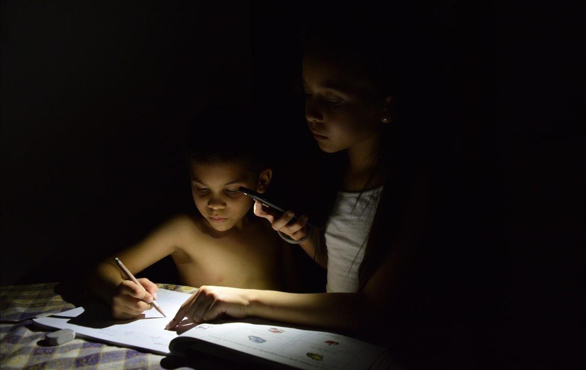 Dos niños estudian alumbrados por la luz de un teléfono, el 21 de abril, en Maracaibo (Venezuela). Norma despacha con rapidez la solicitud de una entrevista. Quiere volver a encerrarse en su habitación y sentir el frío del aire acondicionado durante las ocho horas con electricidad que recibe a diario en Maracaibo, la ciudad venezolana más rica y poblada después de Caracas.