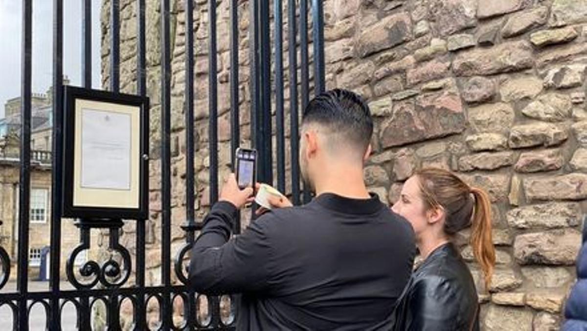 Una pareja fotografía el comunicado sobre la muerte de Isabel II colgado a las puertas del palacio de Holyrood, este viernes en Edimburgo.