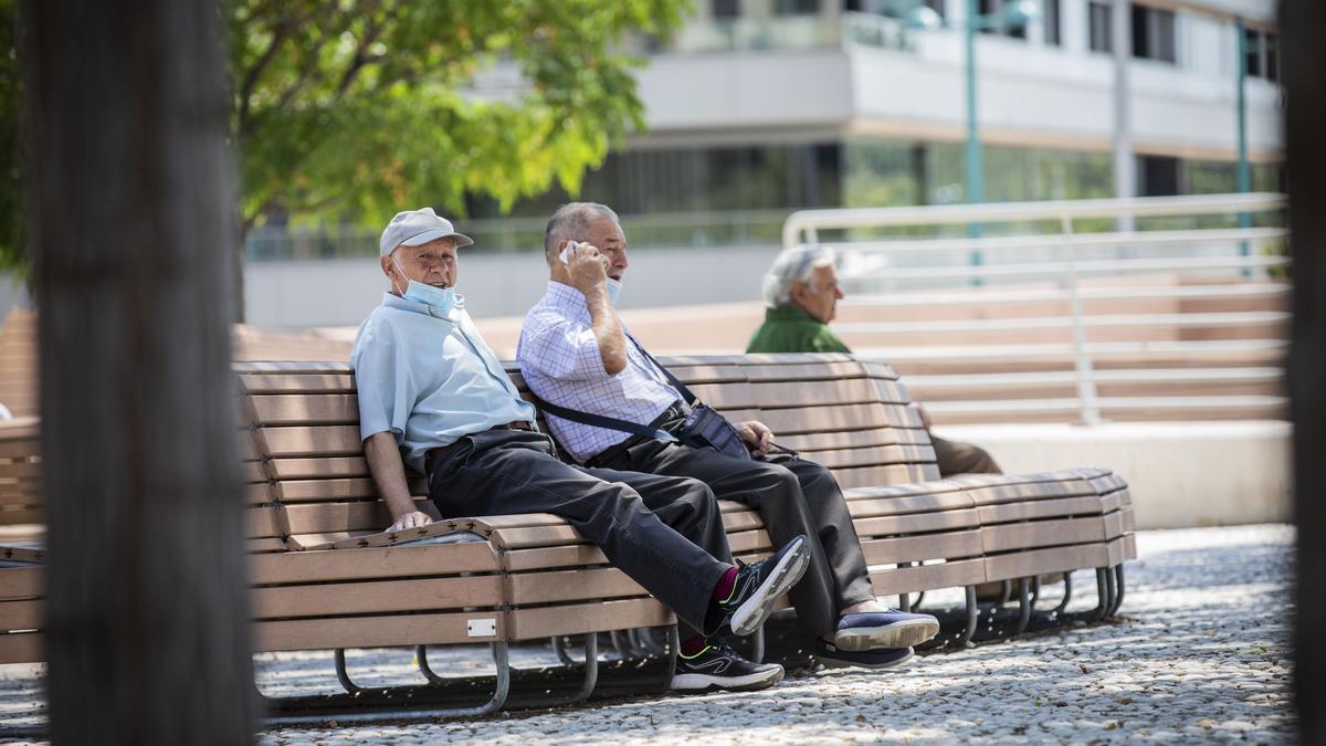 Tres pensionistas descansan en los bancos de una plaza.