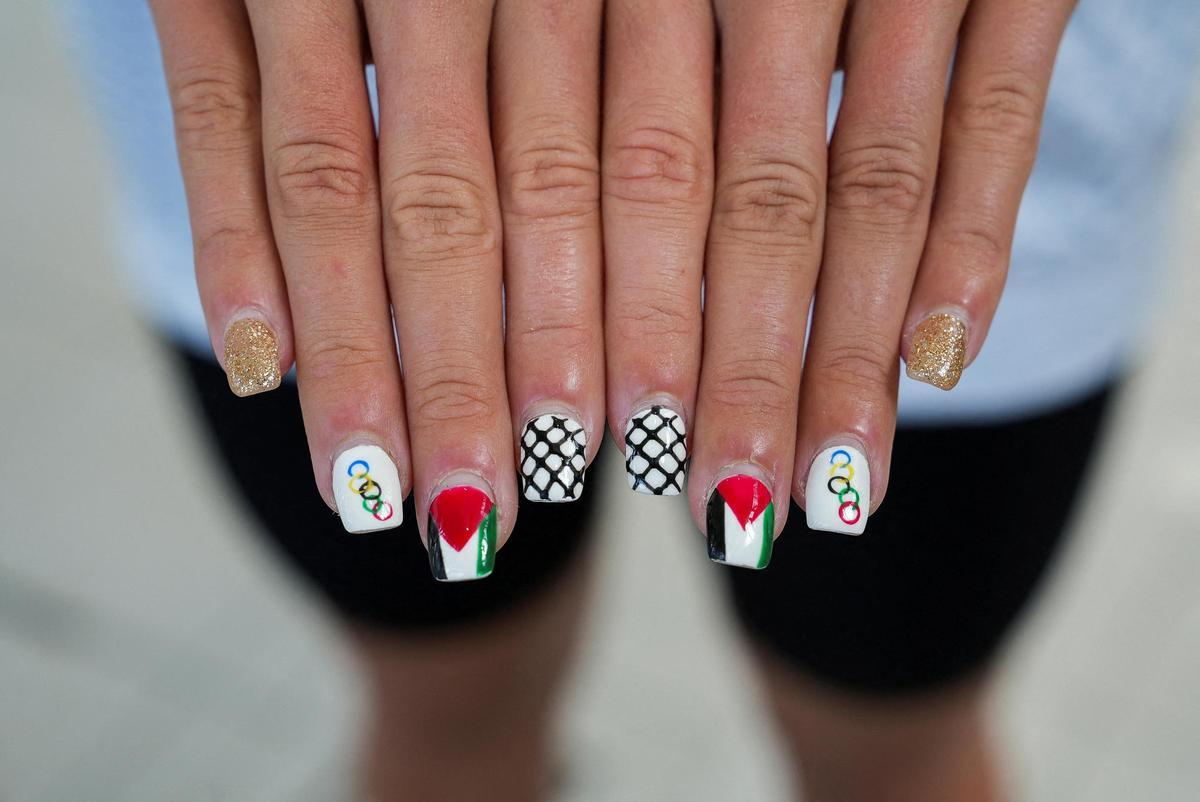 La nadadora palestina Valerie Tarazi muestra sus uñas pintadas con los anillos olímpicos, la bandera palestina y damas blancas y negras antes de los Juegos Olímpicos en París, Francia, el 20 de julio de 2024.