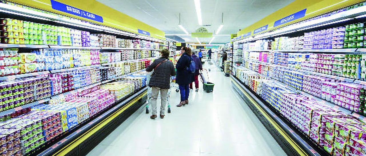 Varios clientes observan la variedad de productos en la sección de yogures en un supermercado.