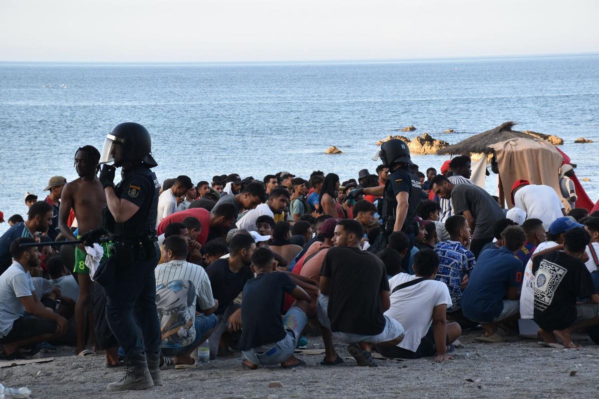 Cientos de migrantes en la playa del Trampolín de Ceuta la semana pasada, ante la presencia de varios policías nacionales antidisturbios.