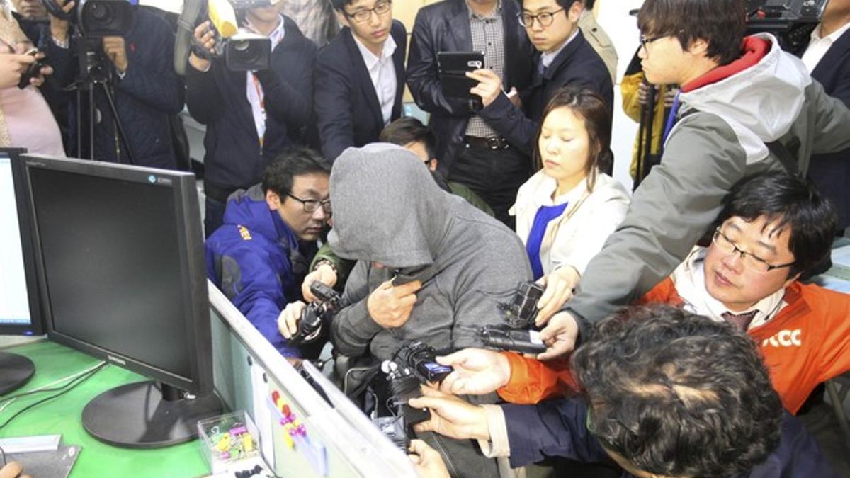 El capitán del 'Sewol', Lee Joon-Seok, con capucha y rodeado de periodistas en la comisaría de Mokpo, este jueves.