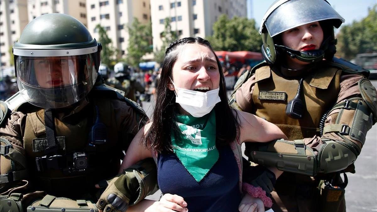 Dos agentes antidisturbios detienen a una joven manifestante en Santiago de Chile.