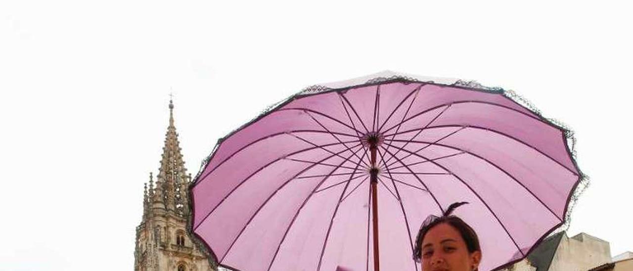 Una actriz y, detrás, una guía turística con un grupo de visitantes en la plaza de la Catedral de Oviedo.