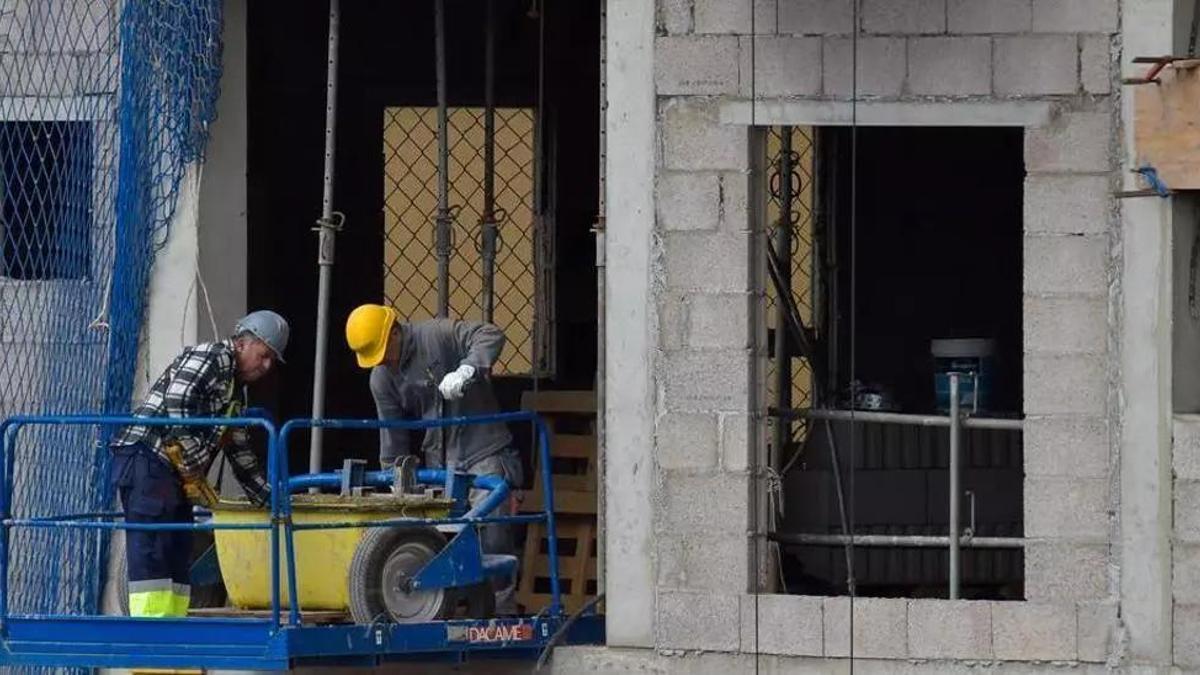 Dos operarios trabajan en la reforma de la fachada de un edificio.