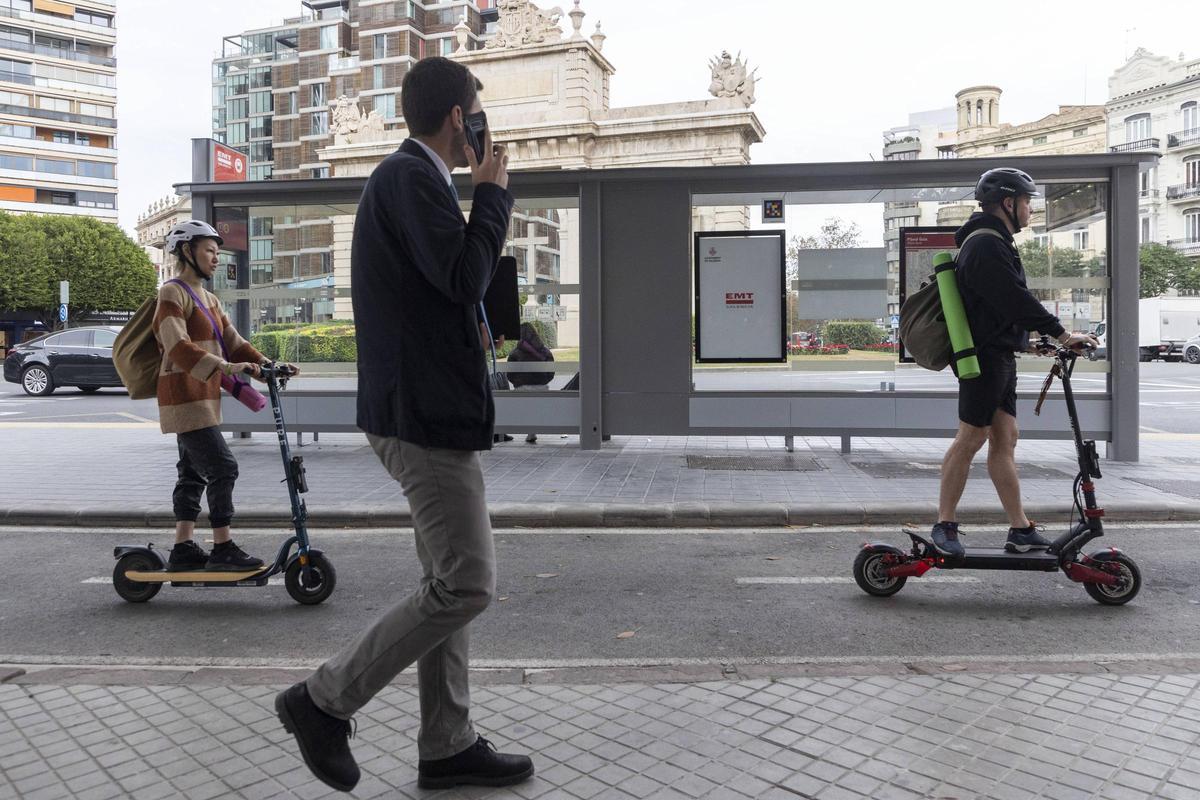 Dos usuarios de patinetes circulan ante una parada de la EMT.