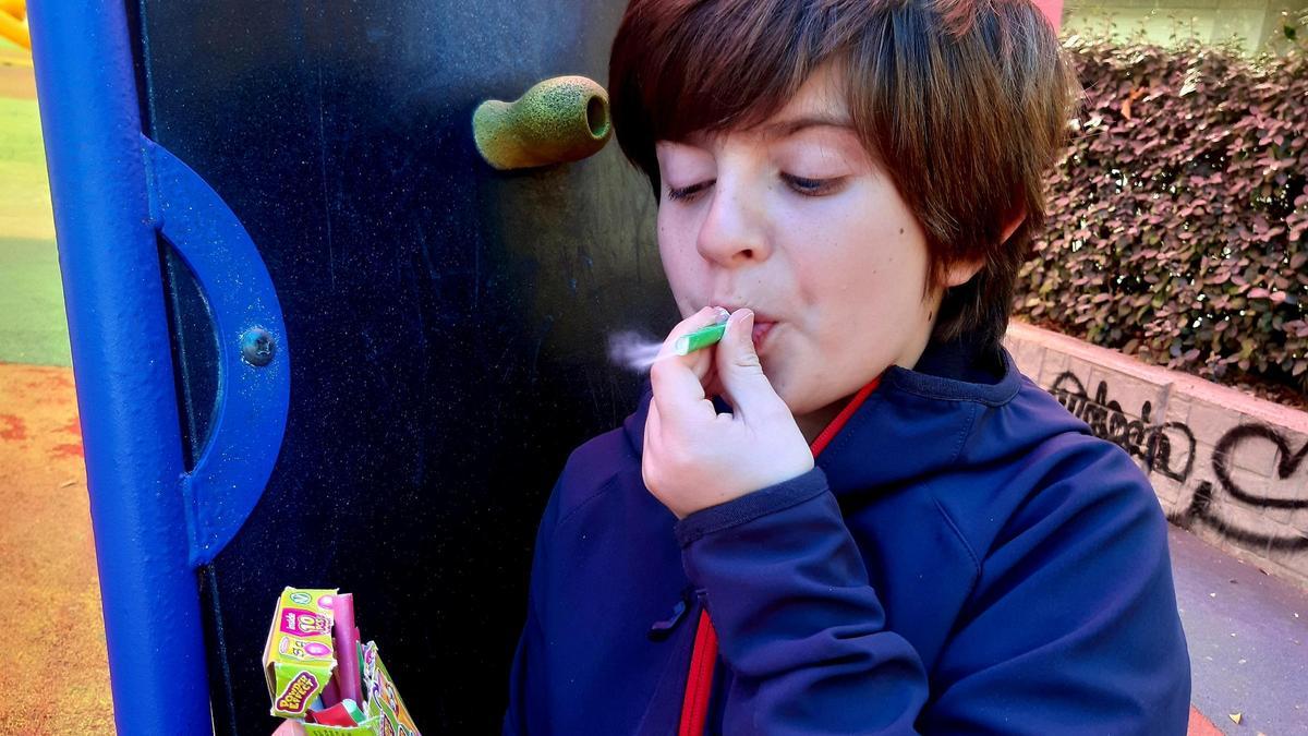 Un niño simula fumar con un chicle-cigarro de efecto humo, en un parque infantil.