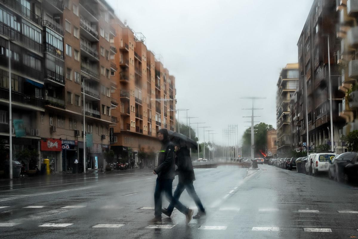 Transeúntes por céntricas calles de Sevilla se protegen de la lluvia.