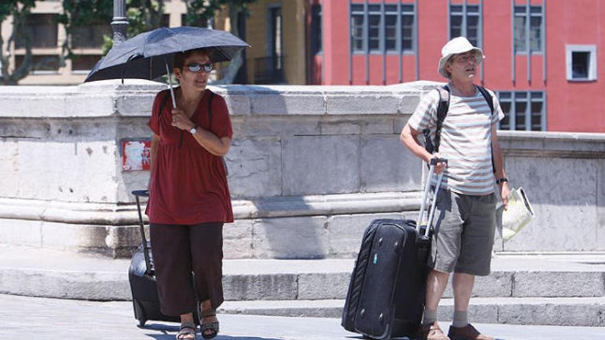 Dos turistes es protegeixen amb paraigües dels intensos rajos de sol a Girona ciutat.