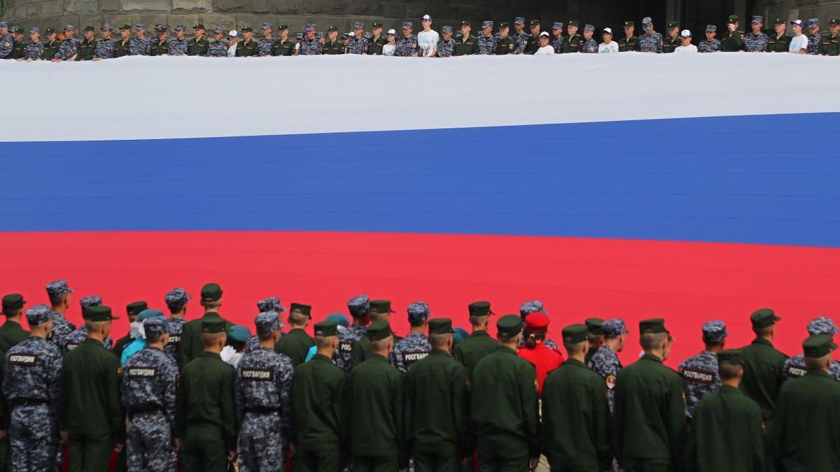 Soldados rusos sostienen una gigantesca bandera, durante el Día de la Bandera Nacional.