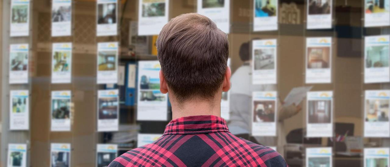 Un joven mira el escaparate de una inmobiliaria ante una escasa y cara oferta de alquileres