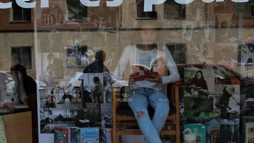 Una joven con su libro lee en el escaparate de la librería de San José Obrero.