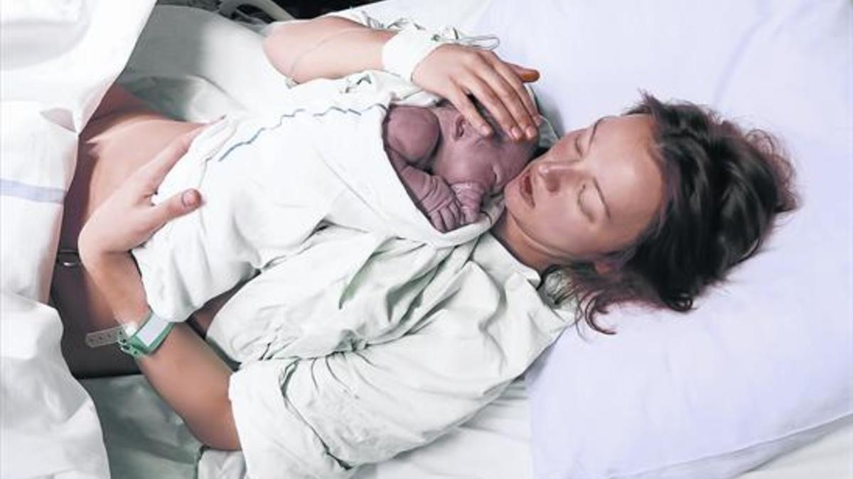Una mujer acaricia a su hijo recién nacido en la cama de un hospital. Tocar al bebé es fundamental tras el parto.