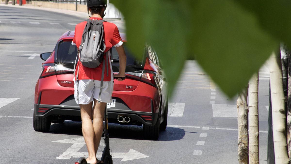 Un joven circula en patinete tras un coche, este lunes en Murcia.