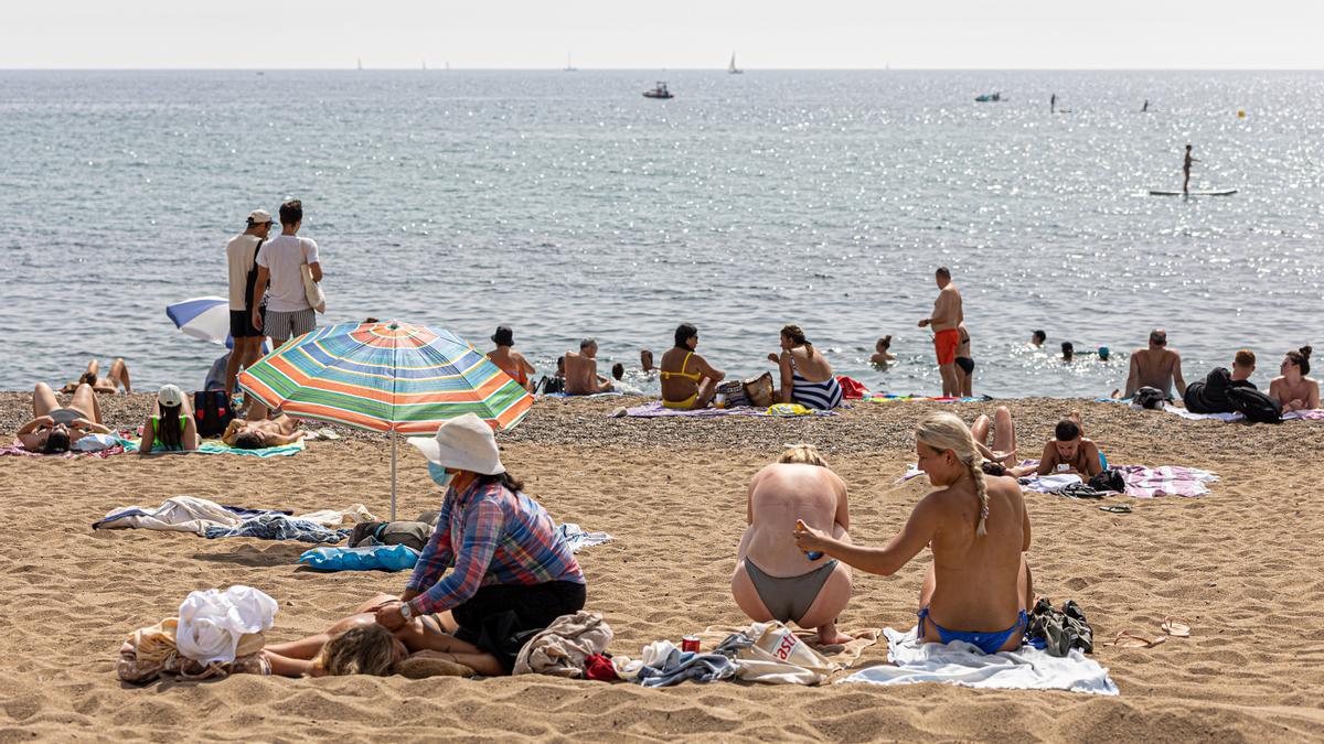 Barcelona 14/07/2021 Sociedad Ola de calor. Una turista pone crema solar a otra mientras una tercera recibe un masaje en la playa de la Barceloneta. AUTOR: JORDI OTIX