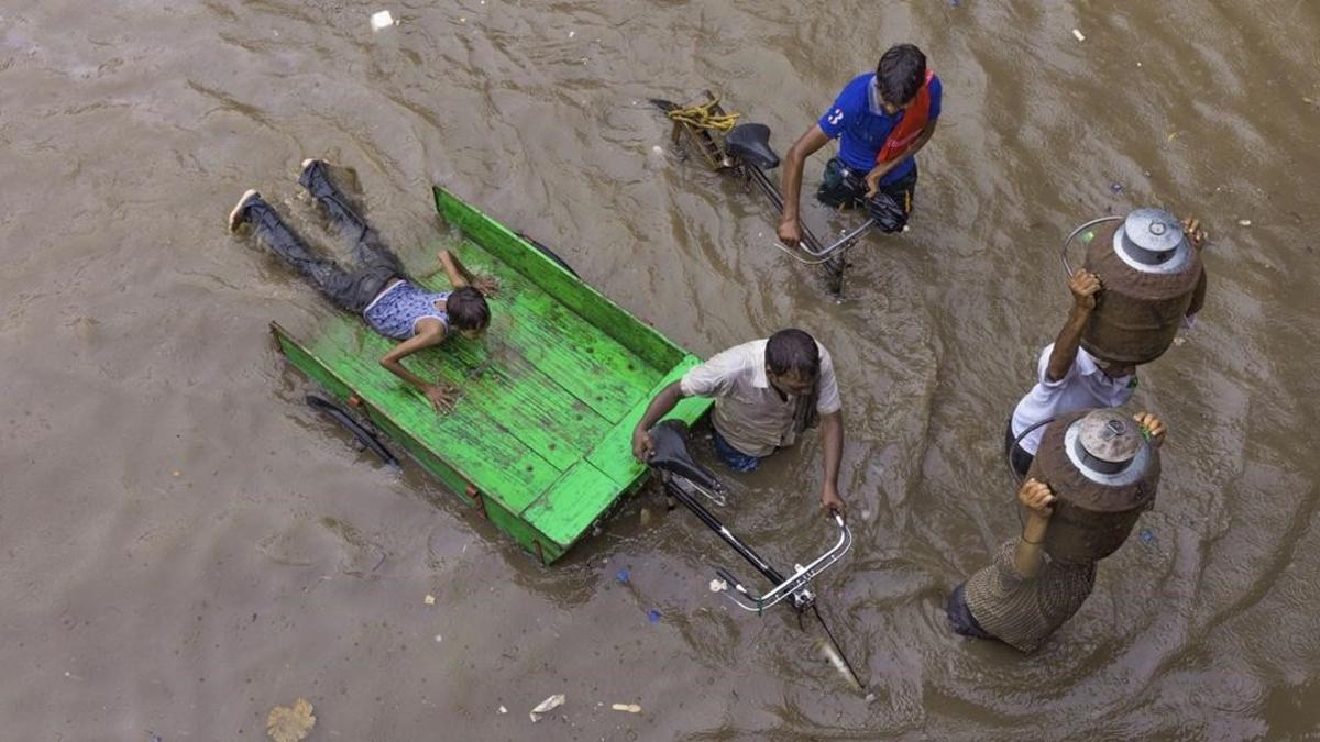 Lecheros intentan abrirse paso por una calle inundada tras las fuertes lluvias en Allahabad, India.